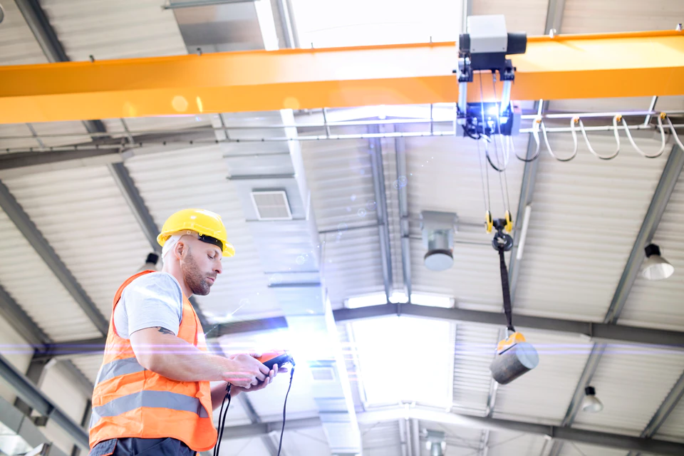 Worker with an overhead crane with lights above illuminating the load