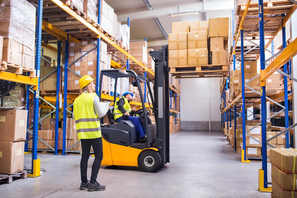 Forklift lifting boxes in a small warehouse with a safety officer overlooking